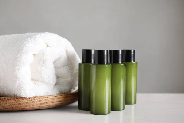 Mini bouteilles avec produits cosmétiques et serviette sur table blanche sur fond gris — Photo