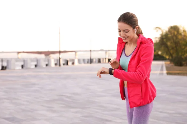 Jeune femme avec écouteurs sans fil et smartwatch écouter de la musique à l'extérieur. Espace pour le texte — Photo