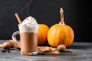 Krem şantili balkabağı aromalı latte ve gri masada cam bardakta tarçın çubuğu.