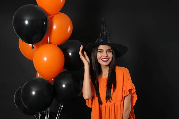 Gyönyörű nő visel boszorkány jelmez léggömbökkel Halloween party fekete háttér — Stock Fotó