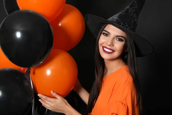 Mulher bonita vestindo traje de bruxa com balões para festa de Halloween no fundo preto — Fotografia de Stock