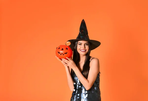 Mulher bonita vestindo traje de bruxa com Jack O 'Lantern recipiente de doces para festa de Halloween no fundo amarelo, espaço para texto — Fotografia de Stock