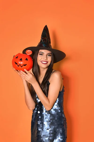 Gyönyörű nő visel boszorkány jelmez Jack O 'Lantern cukorka tartály Halloween party sárga háttér — Stock Fotó