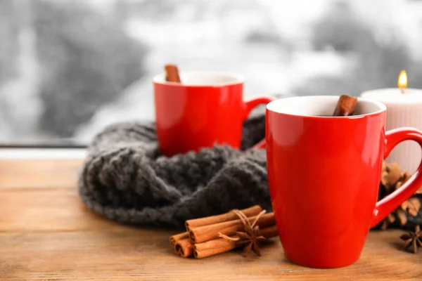 Cups of hot winter drink with scarf on window sill indoors — Stock Photo, Image