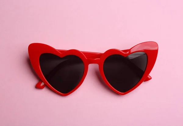 Stylish heart shaped sunglasses on pink background, top view. Fashionable accessory