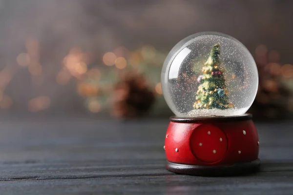 Snow globe with Christmas tree on grey wooden table against festive lights, space for text