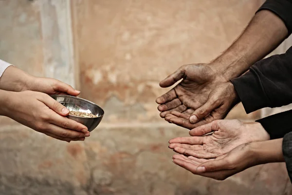 Woman giving poor homeless people bowl of wheat outdoors, closeup