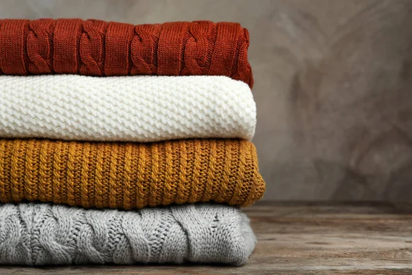 Stapel warme kleren op houten tafel tegen een grijze achtergrond. Herfstseizoen — Stockfoto