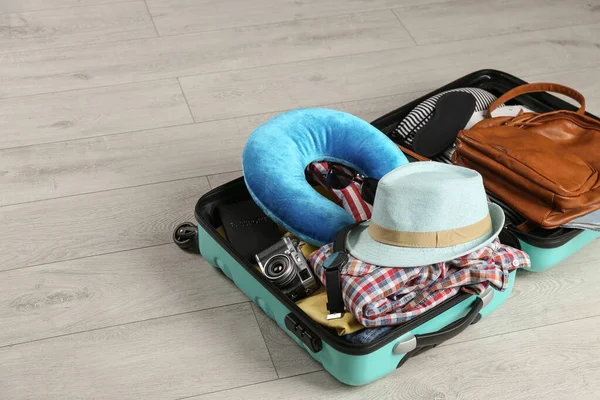 Maleta abierta con almohada de viaje y ropa en suelo de madera — Foto de Stock