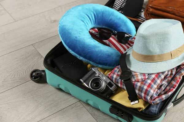 Valigia aperta con cuscino da viaggio e vestiti sul pavimento in legno — Foto Stock