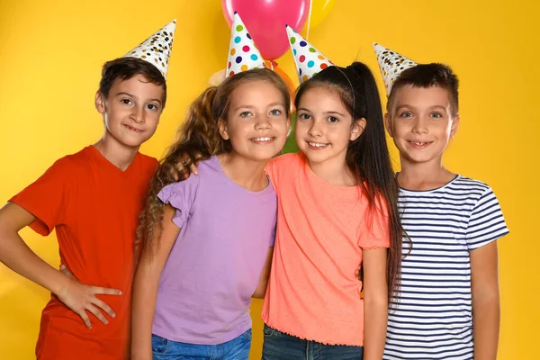 Niños felices en sombreros de fiesta sobre fondo amarillo. Celebración del cumpleaños —  Fotos de Stock