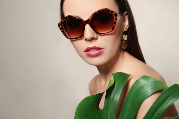Vacker kvinna i snygga solglasögon med tropiskt blad på beige bakgrund — Stockfoto