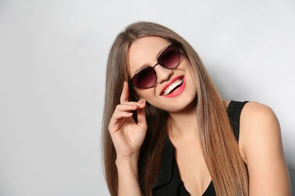 Mujer joven con gafas de sol elegantes sobre fondo claro — Foto de Stock