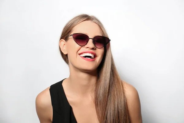 Mujer joven con gafas de sol elegantes sobre fondo claro — Foto de Stock