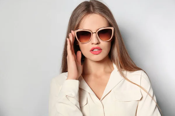 Młoda kobieta w stylowych okularach przeciwsłonecznych na jasnym tle — Zdjęcie stockowe