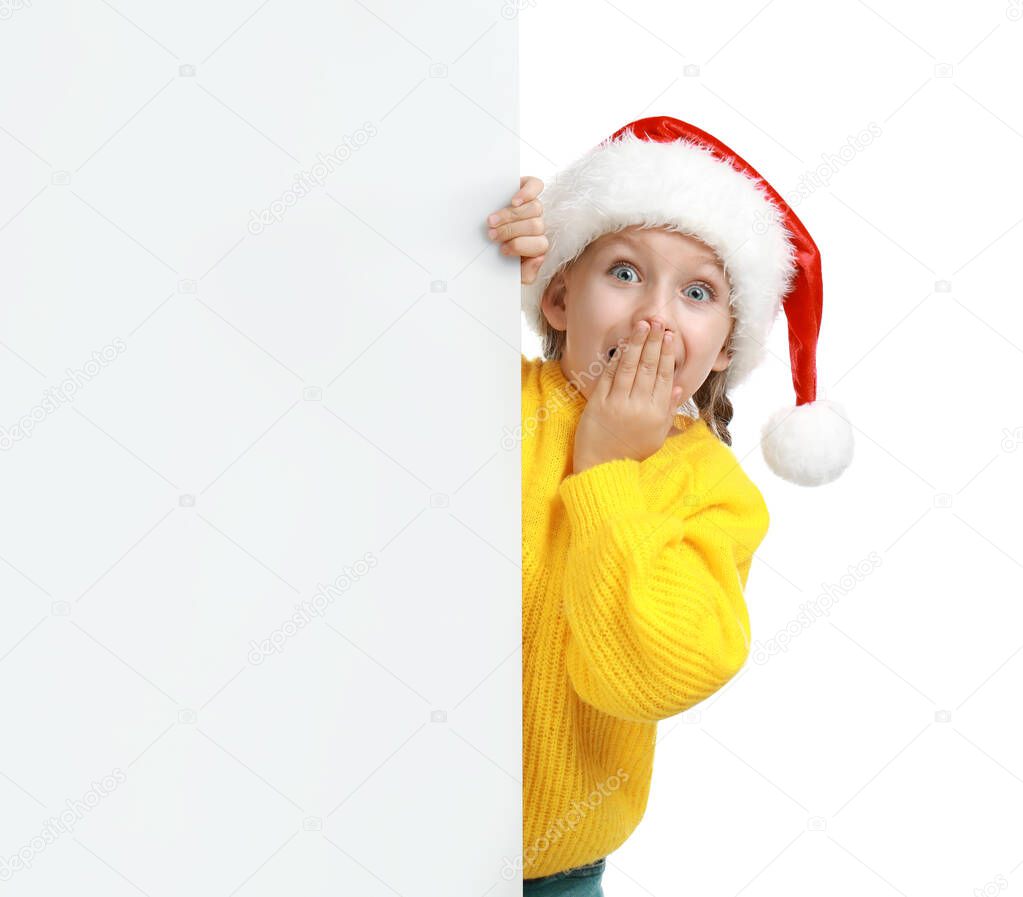 Emotional child in Santa hat peeping out of blank banner on white background. Christmas celebration