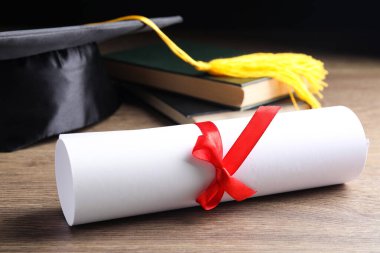 Mezuniyet şapkası, kitaplar ve ahşap masada öğrenci diploması.