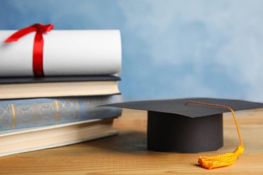 Mezuniyet şapkası, kitaplar ve öğrenci diploması açık mavi arka plana karşı ahşap masada.