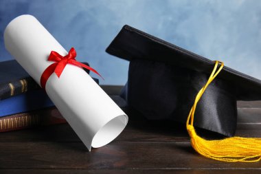 Mezuniyet şapkası, kitaplar ve öğrenci diploması açık mavi arka plana karşı siyah ahşap masa üzerinde
