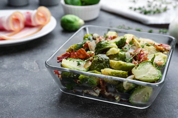 Heerlijke spruitjes met spek in glazen bakvorm op grijze tafel — Stockfoto