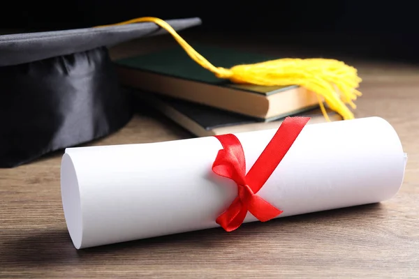 Graduation hat, books and student's diploma on wooden table — Stock Photo, Image