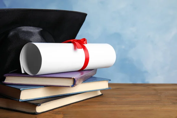 Afstudeerhoed, boeken en studentendiploma op houten tafel tegen lichtblauwe achtergrond — Stockfoto