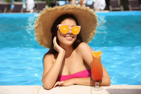 Vacker ung kvinna med cocktail i poolen. Fruktsolglasögon som sommartrend — Stockfoto