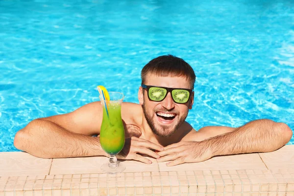 Giovane con cocktail in piscina nella giornata di sole. Occhiali da sole di frutta come tendenza estiva — Foto Stock