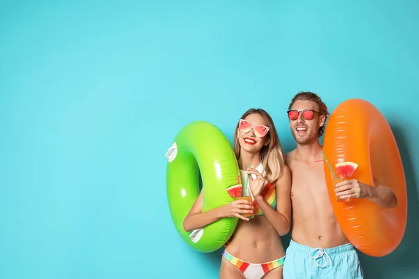 Feliz pareja joven en ropa de playa con anillos inflables y cócteles sobre fondo azul, espacio para el texto. Gafas de sol de frutas como tendencia de verano — Foto de Stock