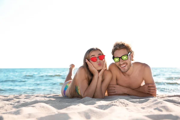 Pareja joven y feliz con gafas de sol en la playa. Gafas de sol de frutas como tendencia de verano — Foto de Stock