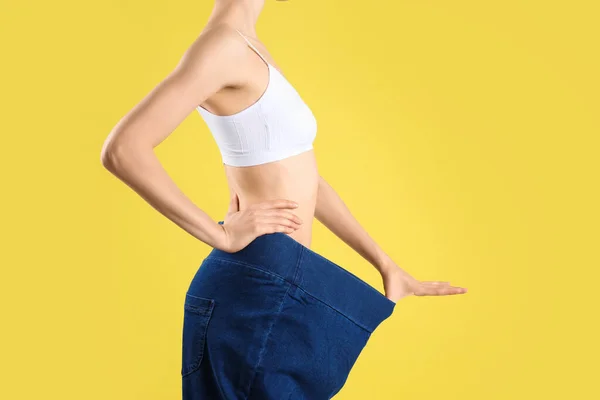 Young slim woman wearing oversized jeans on yellow background, closeup — Stock Photo, Image