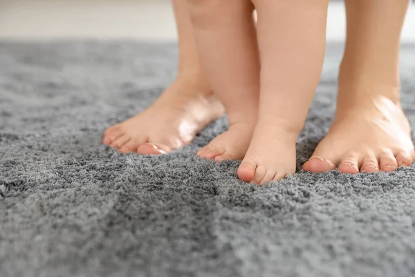 Madre y su bebé de pie sobre la alfombra, primer plano de las piernas — Foto de Stock