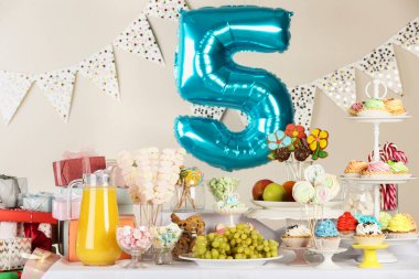 Masanın üzerinde beş numaralı mavi balon. İçerideki doğum günü partisinde leziz ikramlar.