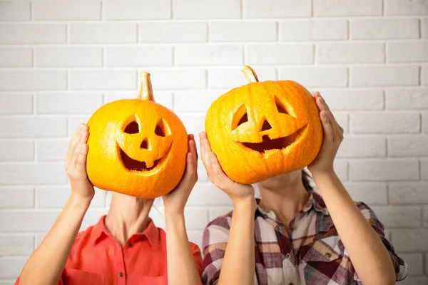 Mulheres com cabeças de abóbora perto da parede de tijolo branco. Lanterna de Jack - decoração de Halloween tradicional — Fotografia de Stock