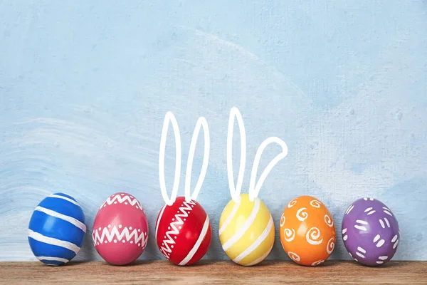 Uova di Pasqua decorate e orecchie di coniglietto carino sul tavolo contro lo sfondo di colore. Spazio per testo — Foto Stock