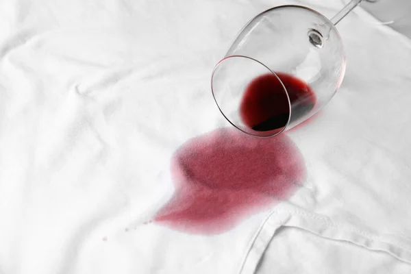 Umgekipptes Glas und verschütteter Rotwein auf weißem T-Shirt. Raum für Text — Stockfoto