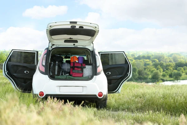 Car with camping equipment in trunk on green field. Space for text — Stock Photo, Image