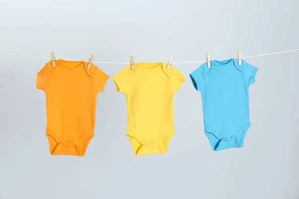 Різні дитячі онезії висять на лінії одягу на світло-сірому тлі. День прання — стокове фото