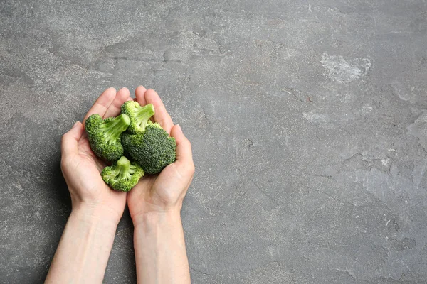 Perempuan memegang brokoli hijau segar di meja batu abu-abu, pemandangan atas. Ruang untuk teks — Stok Foto