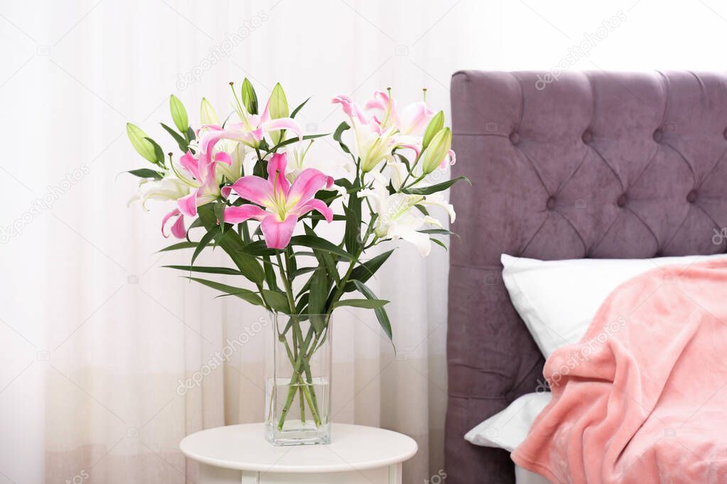 Vase with bouquet of beautiful lilies on table in bedroom. Space for text