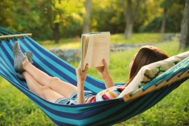 Yeşil bahçedeki hamakta kitap okuyan genç bir kadın.