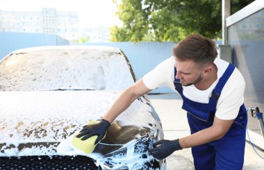 Araba yıkamada süngerle otomobili temizleyen genç işçi.