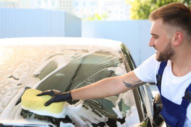 Araba yıkamada süngerle otomobili temizleyen genç işçi.