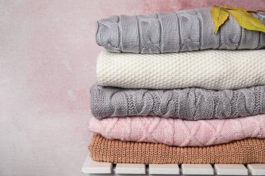 Pembe arka plana karşı beyaz ahşap masa üzerinde kalın örülü giysiler ve sonbahar yaprakları yığını