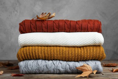 Kalın giysi yığını ve sonbahar yaprakları gri arka plana karşı ahşap masada.