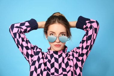 Mavi arka planda şık güneş gözlüğü takan genç bir kadın.