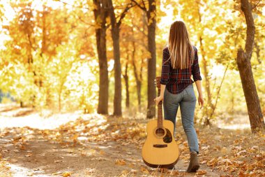 Sonbahar parkında akustik gitarlı genç bir kız.