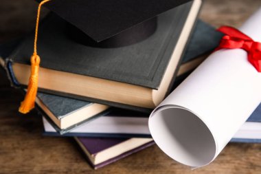 Mezuniyet şapkası, kitaplar ve öğrenci diploması ahşap masada, yakın plan.