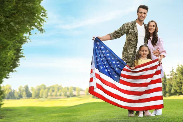 Homem de uniforme militar com bandeira americana e sua família no parque ensolarado — Fotografia de Stock