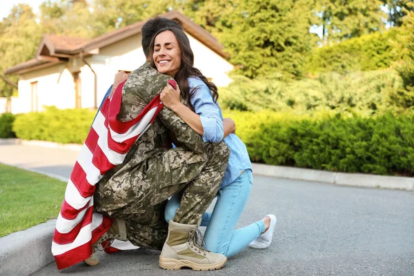 Homem de uniforme militar com bandeira americana abraçando sua esposa ao ar livre — Fotografia de Stock